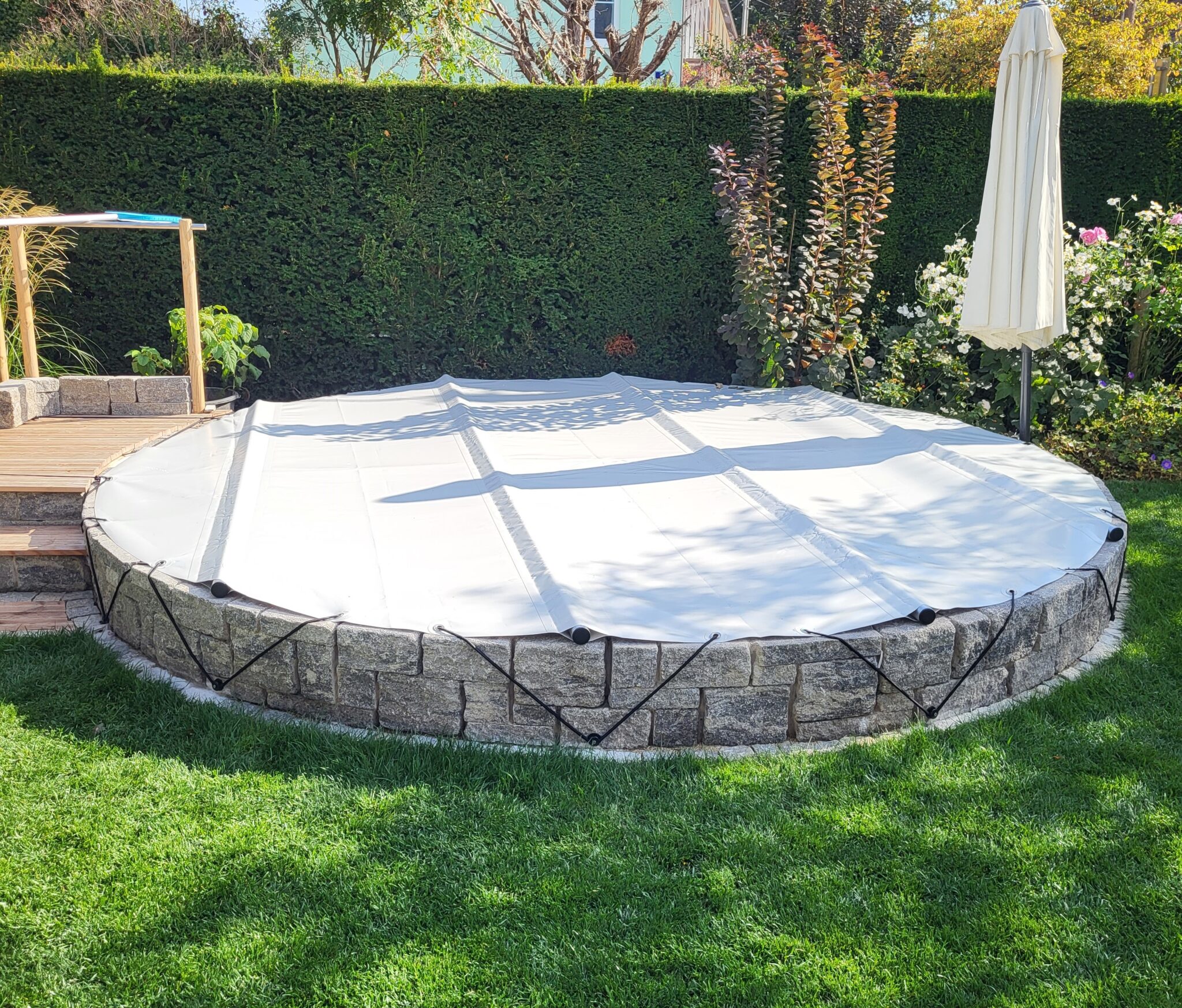Der runde Pool verfügt über eine sichere, weiße Sicherheitsabdeckung, die über eine Steinmauer gespannt ist.