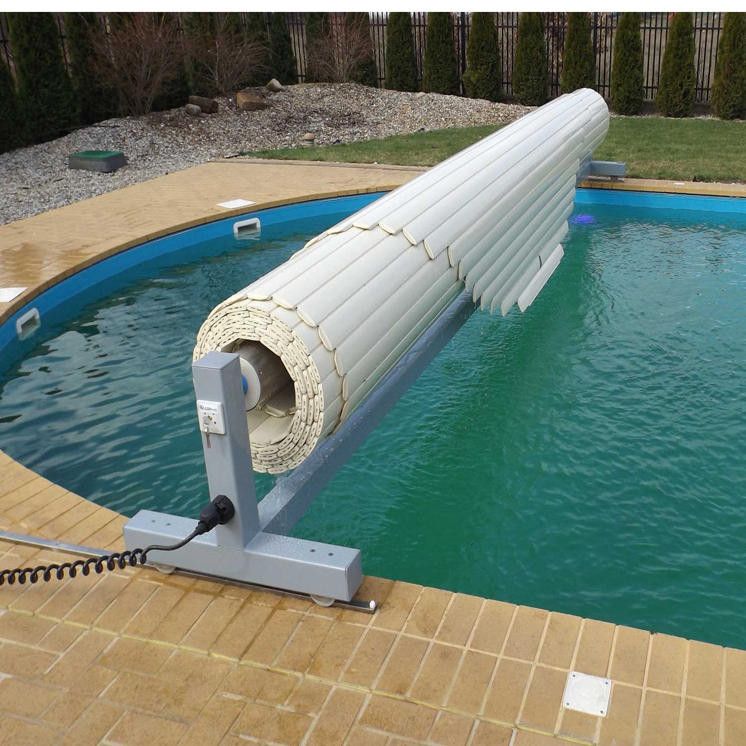 Das automatische Poolabdeckungssystem ist teilweise eingefahren und gibt den Blick auf blaues Wasser im Pool frei. Eine Abdeckrolle ist sichtbar.