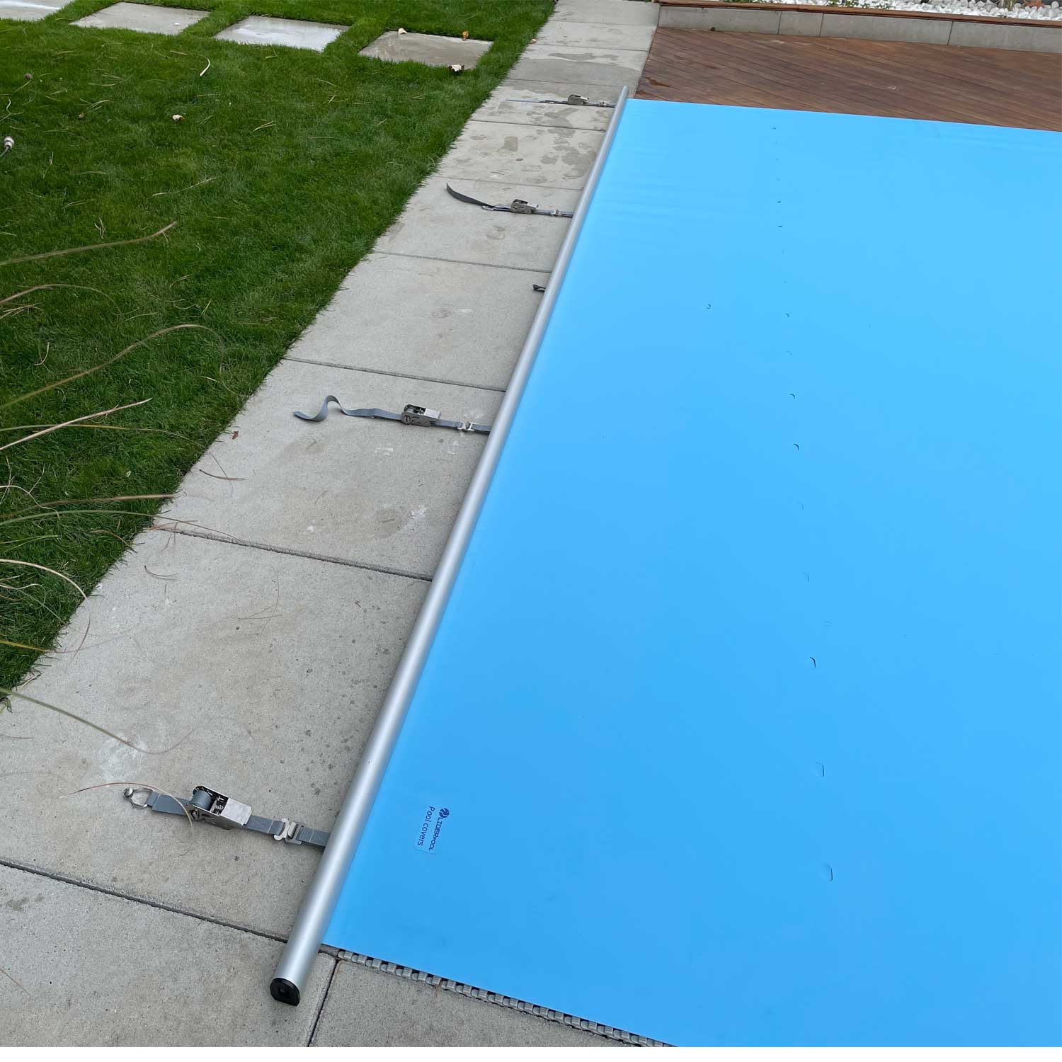 Blaue Poolabdeckung, die sich teilweise über einen Pool erstreckt und Sicherungsgurte und eine Aluminiumstange zeigt.