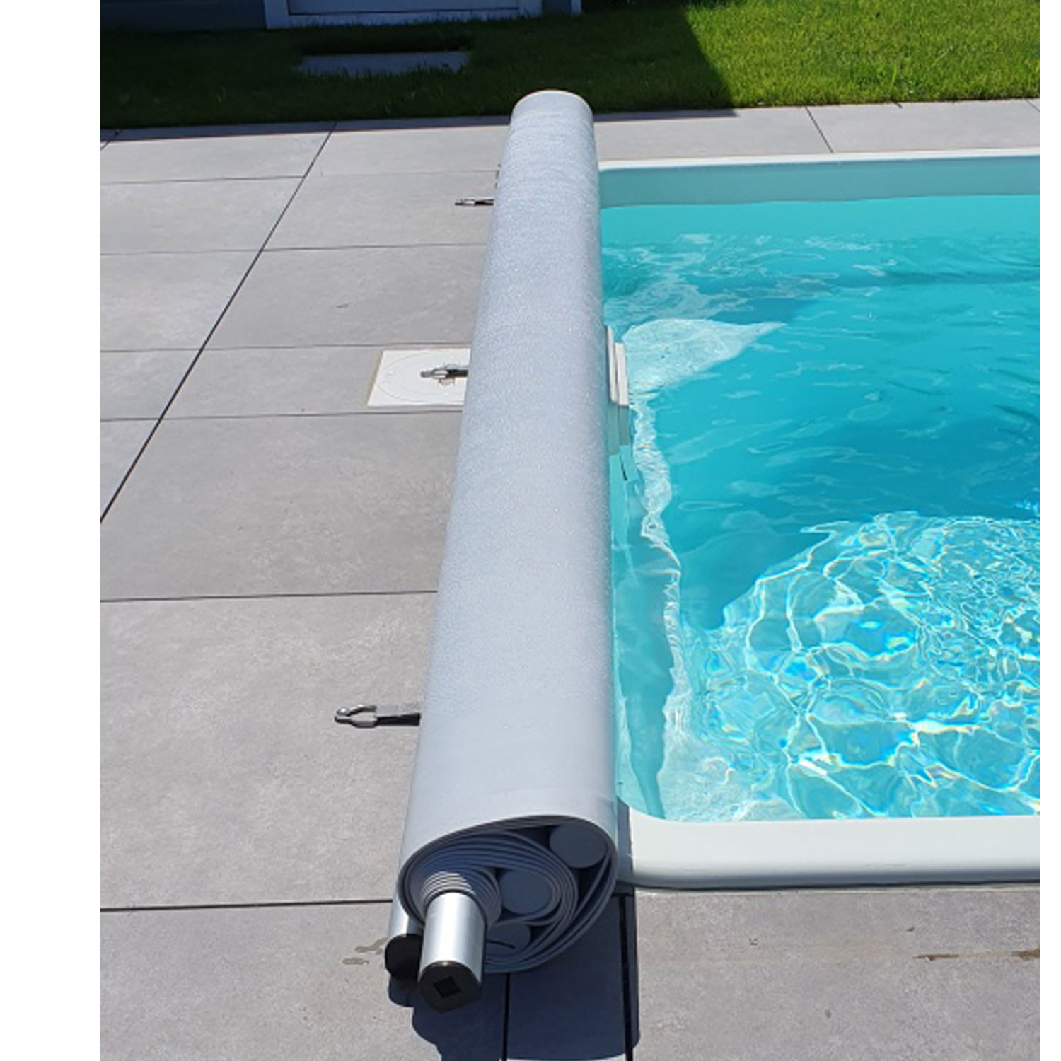 Aufgerollte Sicherheits-Poolabdeckung auf dem Deck neben dem Beckenrand. Die Abdeckung wird mit Haken befestigt.