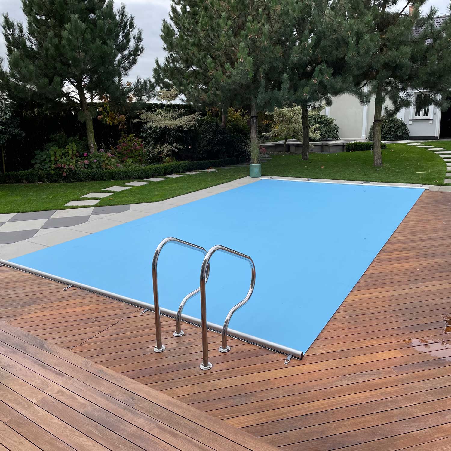 Blick auf einen rechteckigen Swimmingpool mit einer soliden blauen Sicherheitsabdeckung und einer Edelstahlleiter.