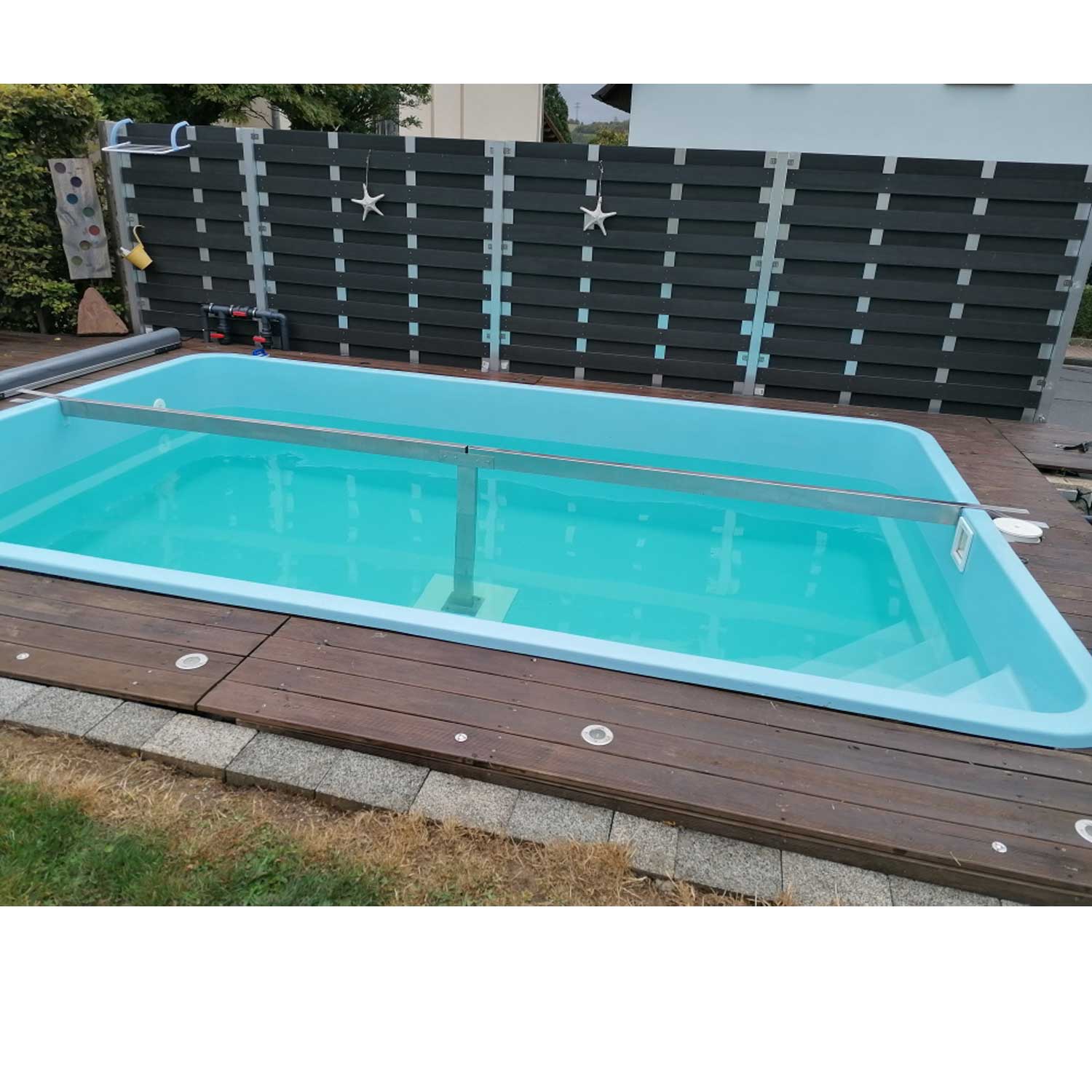 Rechteckiger Swimmingpool mit türkisfarbenem Wasser, Sicherheitsabdeckung und Holzterrassenumrandung.