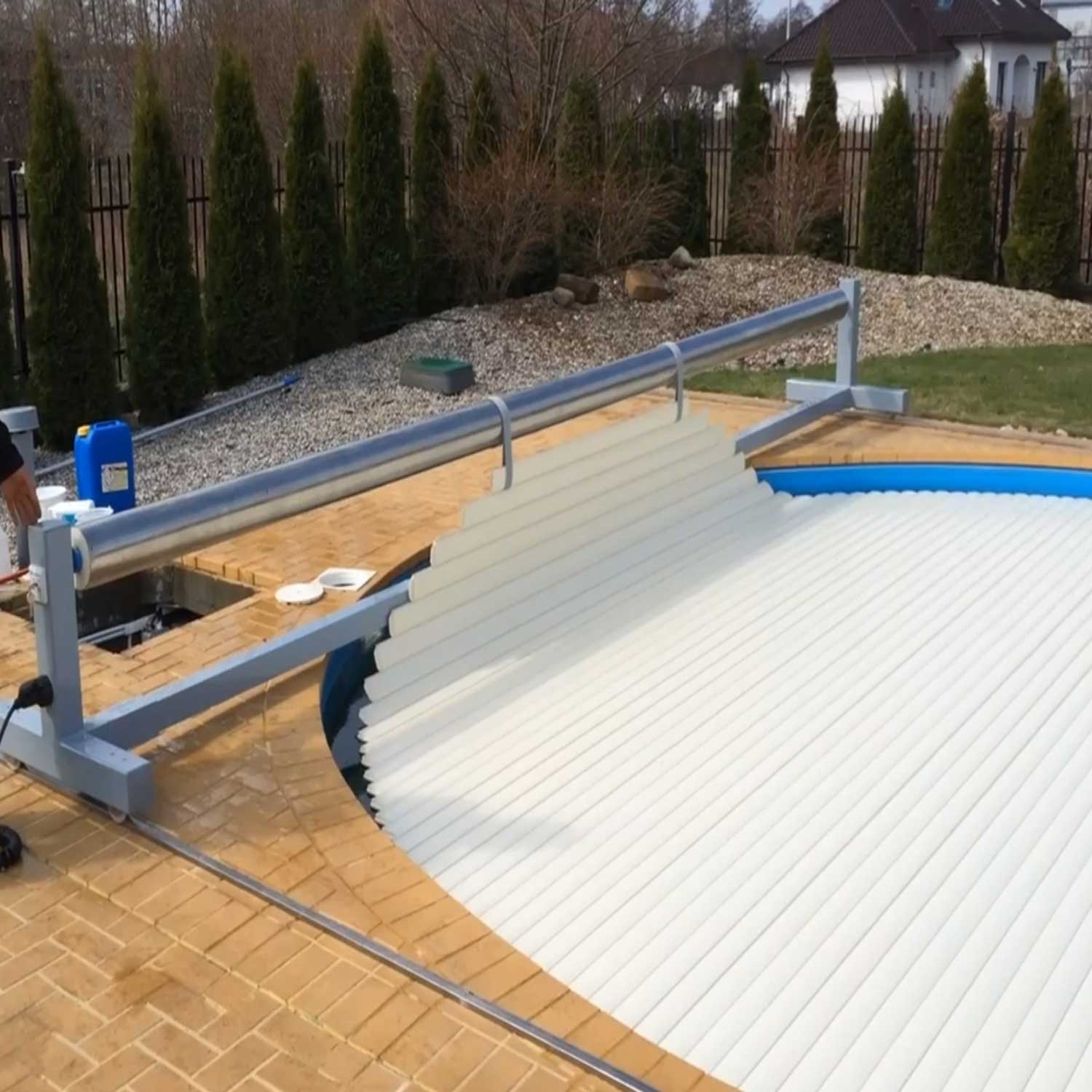 Automatisiertes Poolabdeckungssystem mit einer weißen, teilweise eingefahrenen Lamellenabdeckung, installiert auf einer gemauerten Abdeckung.