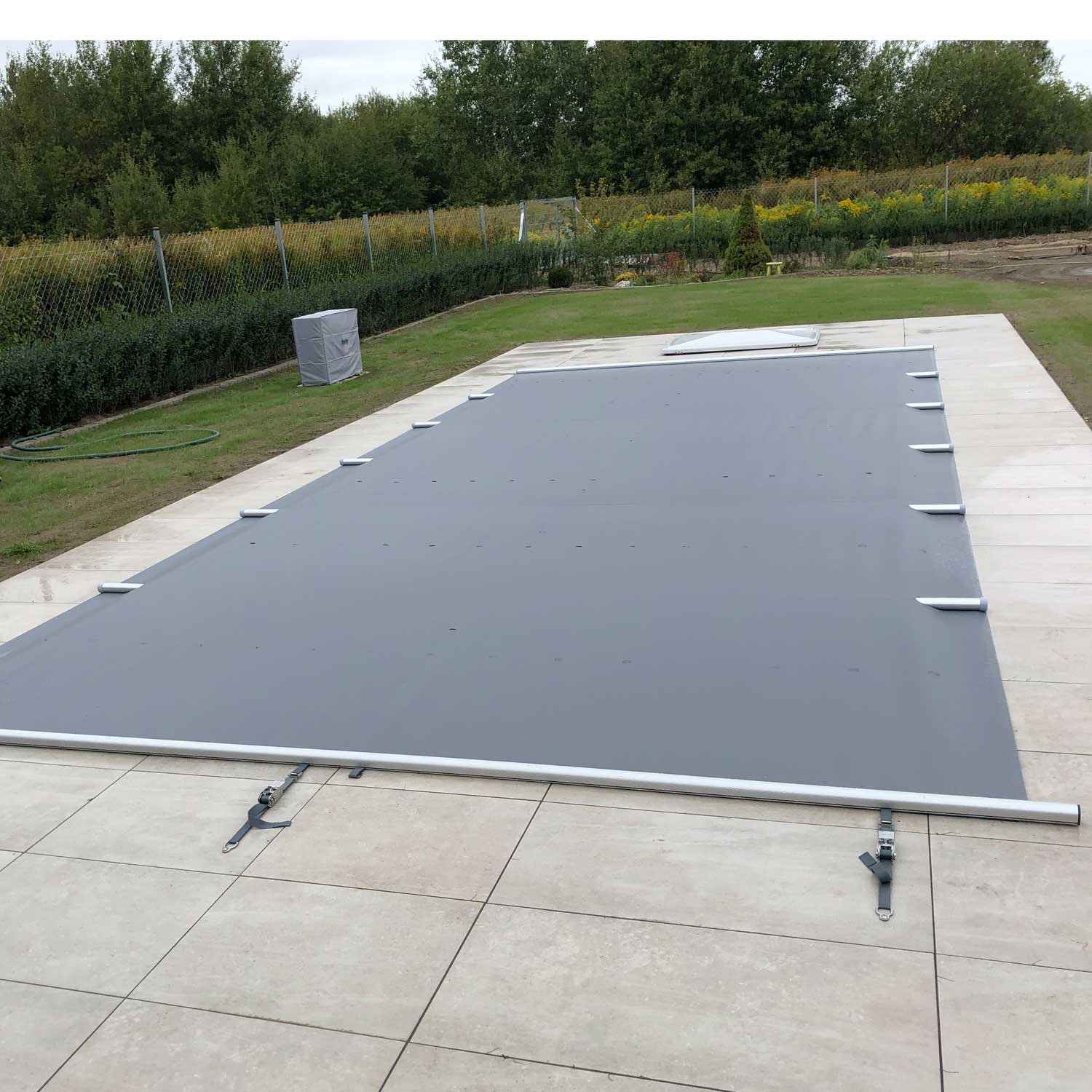 Rechteckiger Pool mit grauer Sicherheitsabdeckung und hellgrauer Steinflieseneinfassung.