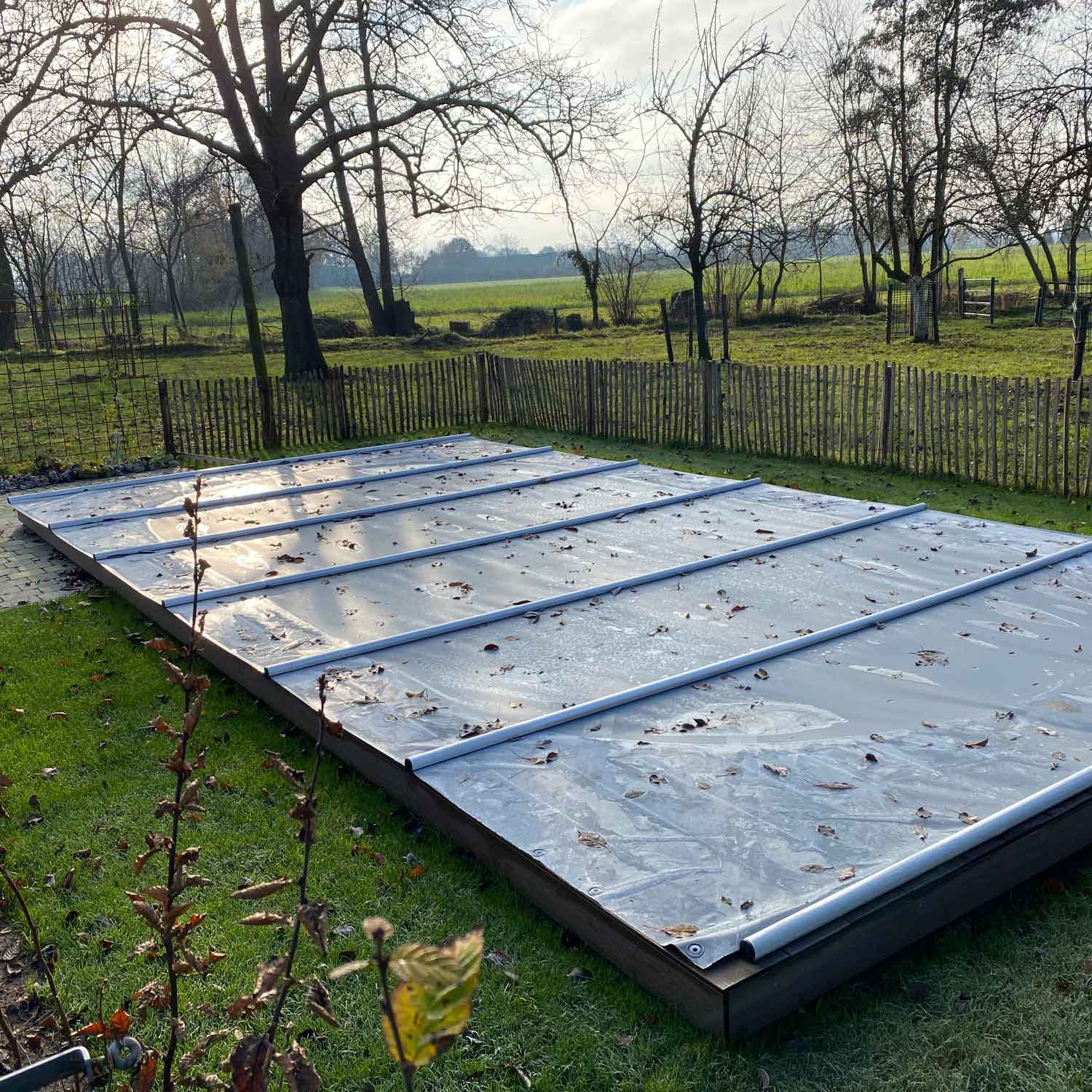 Rechteckiger Pool mit Winterschutzabdeckung. Die Abdeckung ist über die gesamte Breite mit Metallstützen versehen.