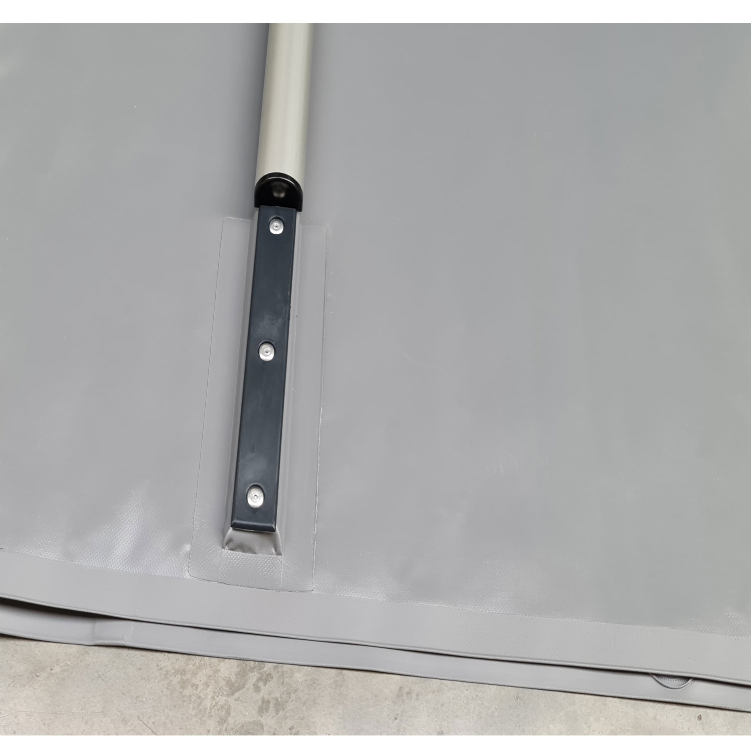 Das Bild zeigt die Nahaufnahme der grauen Poolabdeckung mit Metallstange und Befestigungsmaterial.