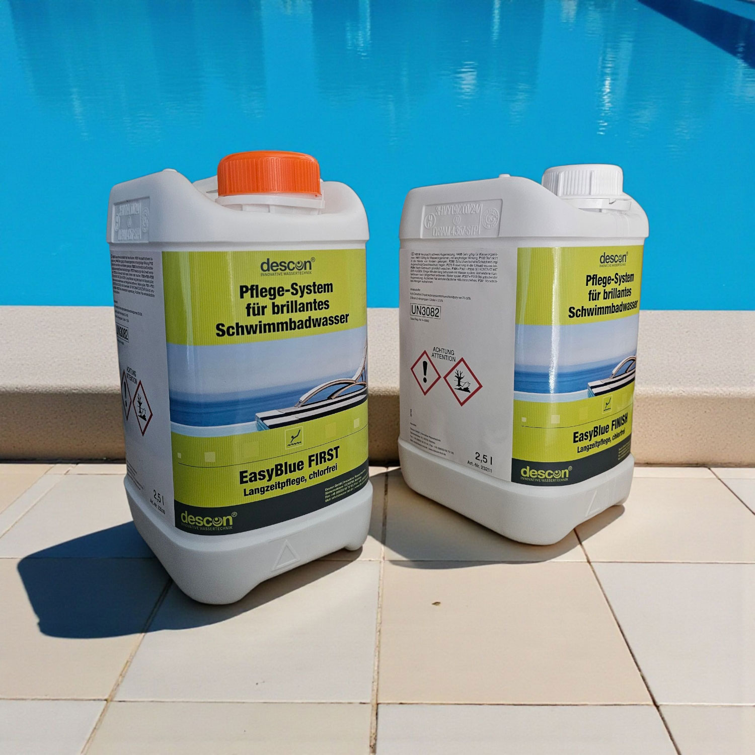 Zwei weiße Behälter mit Descon EasyBlue Poolpflegeprodukten stehen in der Nähe eines Pools.