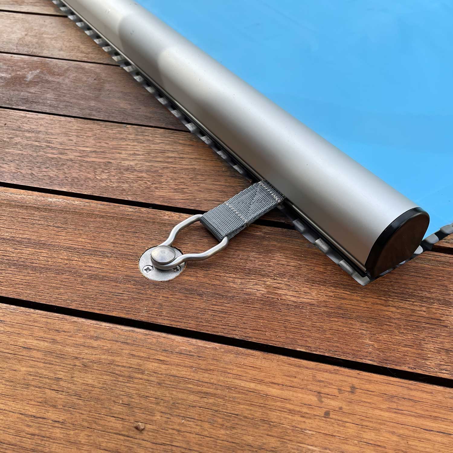 Detail einer Schwimmbadabdeckung mit Metallsicherungsmechanismus auf einem Holzdeck.