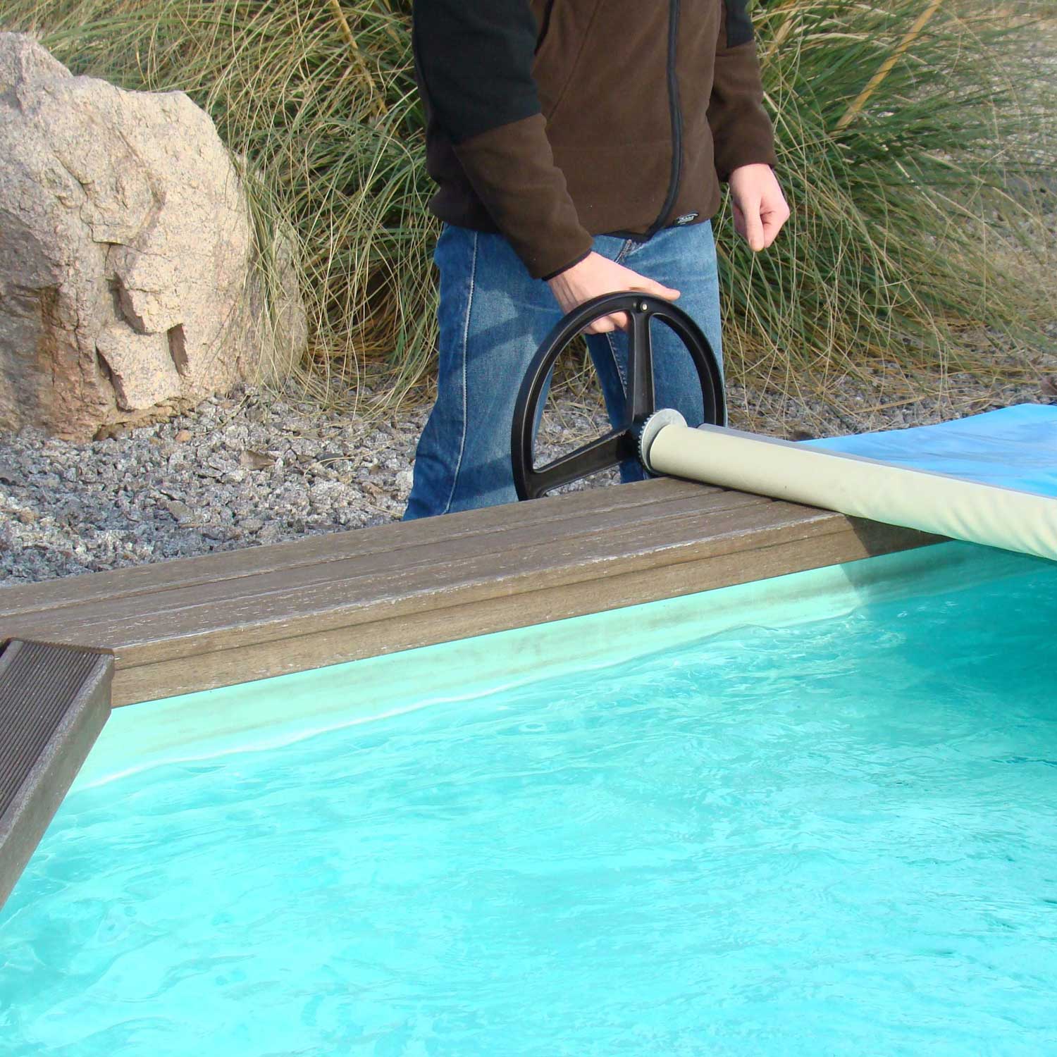 Ein Bediener verwendet eine Haspel mit Handrad, um die einziehbare Pool-Sicherheitsabdeckung zu bedienen.